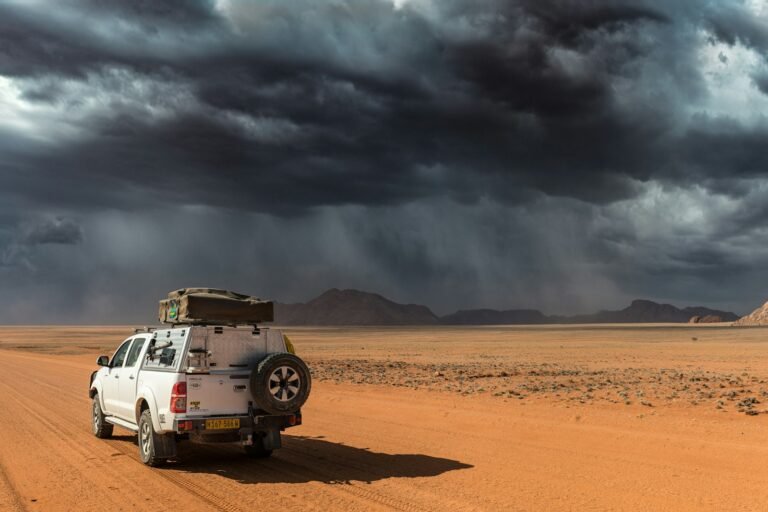 Pick-up avec tente de toit sur une piste de gravier du désert namibien, sous un ciel d’orage